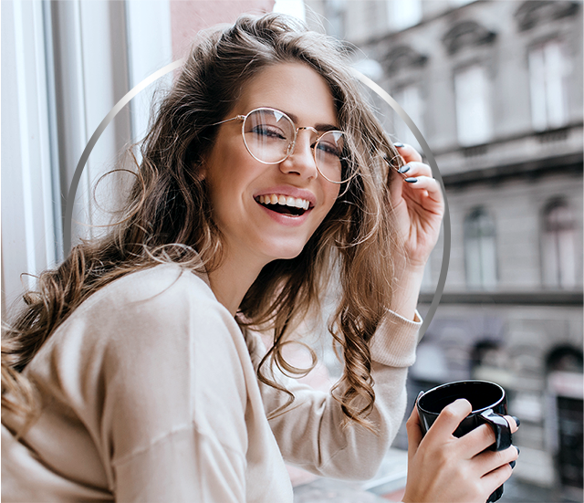 Laughing young blonde girl in glasses holding cup, happy after Canesten cystitis treatment