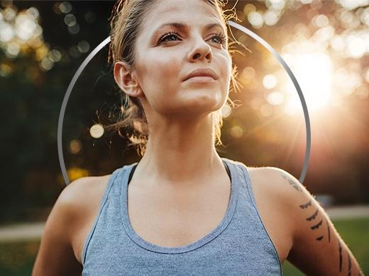 Active young woman wearing tank top and standing in empowered pose against a sunny backdrop